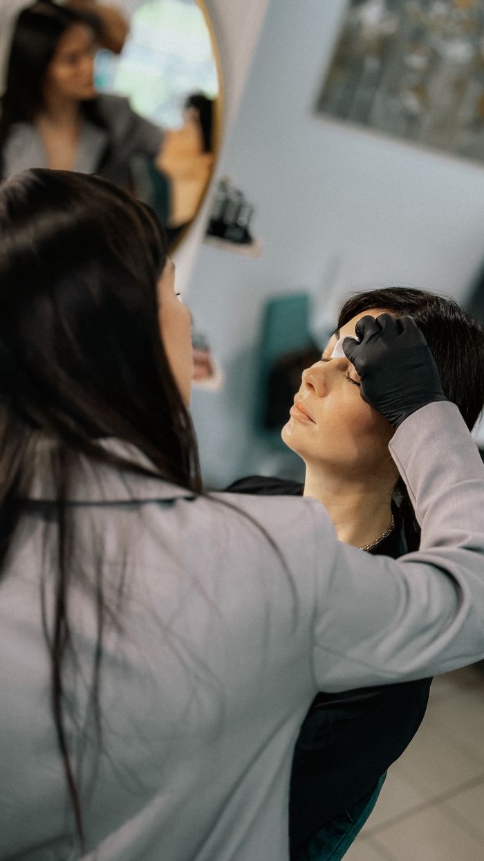 Makeup artist carefully applying eyebrow makeup to client in a salon.